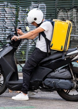 Genç kurye, teslimatçı caddedeki bir motosiklette termo sırt çantasıyla cep telefonuyla gideceği yeri arıyor. Eve hızlı ulaşım ekspresi. Çevrimiçi düzen