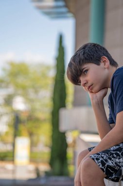 Ciddi bir çocuk bir sorun üzerinde düşünüyor ve çitin üzerinde oturmayı düşünüyor. Gerçek insanlar konsepti.