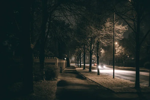 Dark snowy footpath close to a road and a car is approaching — Stock Photo, Image