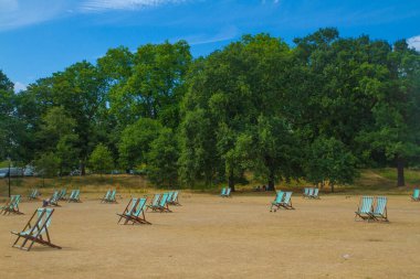 Hyde Park, Londra, İngiltere: güneş pansiyonlu yeşil bir yaz parkı manzarası, parktaki bir dinlenme alanı, parktaki ahşap sandalyeler, yazın park şehri