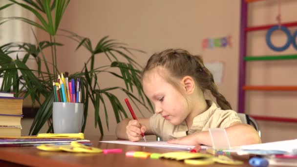 Malá školačka dělá domácí úkoly. Školka dítě píše s perem sedí u stolu. — Stock video