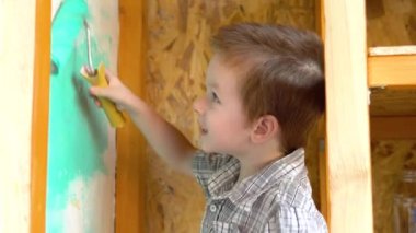 Küçük yakışıklı çocuk duvarı yeşil bir tekerlekle boyuyor. Duvara boya bulaştırıyor..