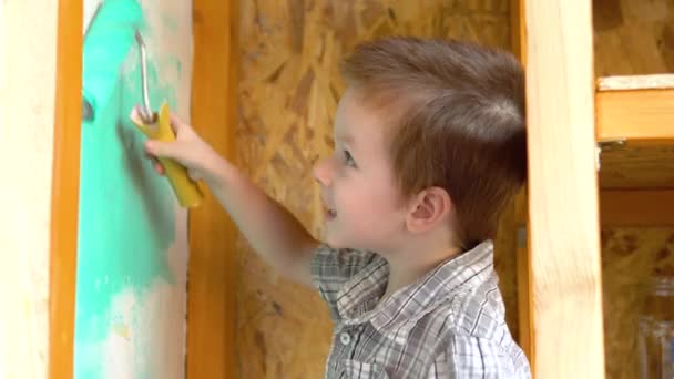 Der kleine, gutaussehende Junge bemalt die Wand mit einem Roller grün. Er schmiert Farbe an die Wand. — Stockvideo