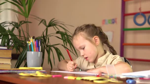 Klein schoolmeisje doet huiswerk thuis. Kleuterschoolkind schrijft met een pen aan tafel. — Stockvideo