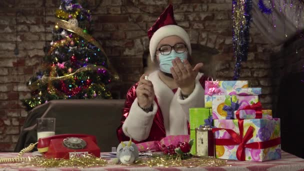 Virüsten koruyucu maskeli Noel Baba ellerine antiseptik sıkar ve bir hediye kutusu alır.. — Stok video