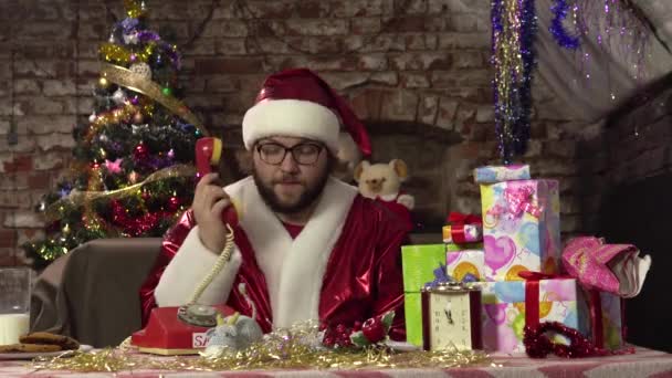 Babbo Natale divertente sta parlando sul vecchio telefono rosso mentre è seduto sul divano. Risponde alla chiamata. — Video Stock