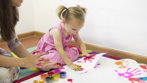 Una joven madre con sus hermosos dibujos de hija con pinturas usando sus dedos. — Vídeos de Stock