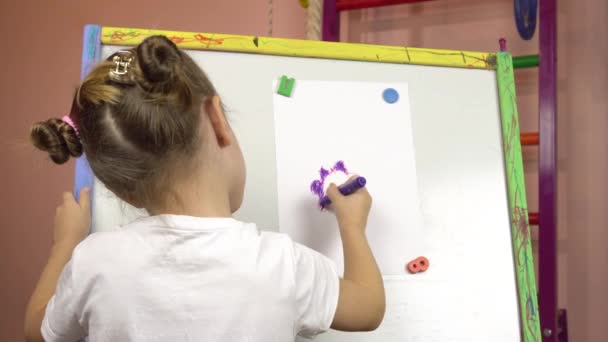 Egy ötéves kislány filctollal rajzol egy virágot egy papírlapra egy állványra.. — Stock videók