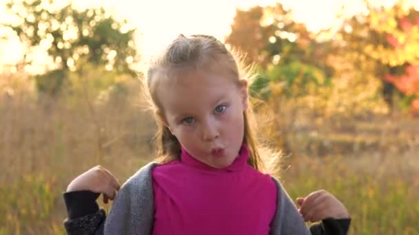 Κορίτσι παιδί στο πάρκο φθινόπωρο κοιτάζει την κάμερα και γκριμάτσες. — Αρχείο Βίντεο