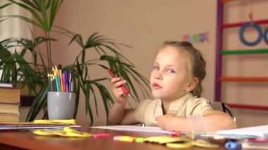 Anaokulu öğrencisi masada otururken düşünüyor. Ödevini yapıyor..