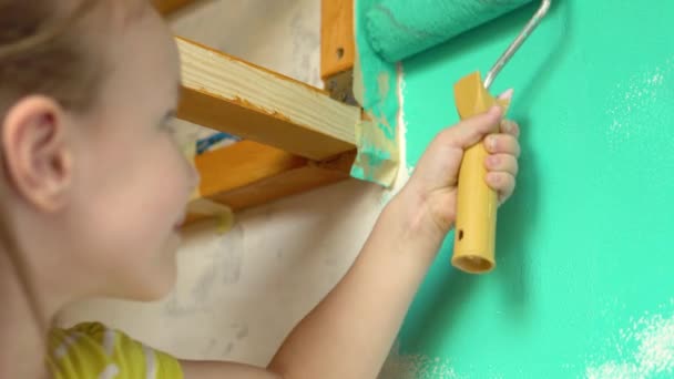 Kleines hübsches Mädchen bemalt die Wand mit einem Roller grün. Sie schmiert die Farbe an die Wand. — Stockvideo