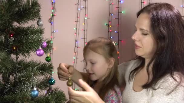 Une belle petite fille avec une jeune mère décore le sapin de Noël. 4k — Video