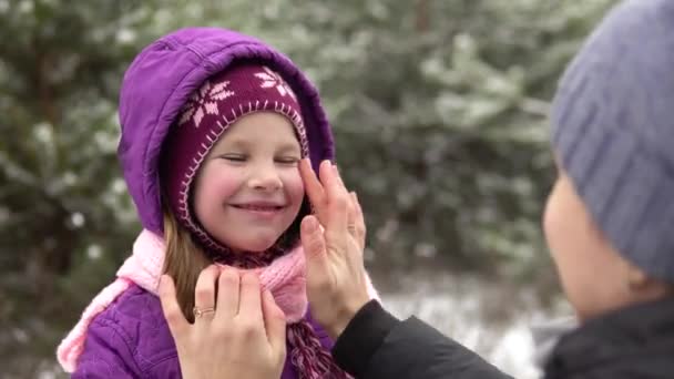Anya kiegyenesít egy meleg kalapot és sálat a kislányán, hogy télen sétáljon egyet.. — Stock videók