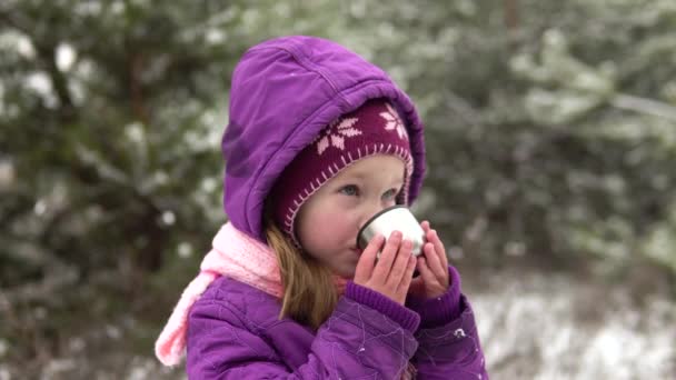En liten flicka i vinterkläder dricker varmt te från en kopp på gatan, ångan går.. — Stockvideo