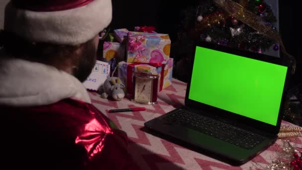 Babbo Natale si siede a un tavolo con un computer portatile, saluta la mano, si congratula.. — Video Stock