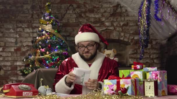 S. Claus est assis à une table avec des cadeaux à la maison et sort une lettre pour enfants d'une enveloppe — Video