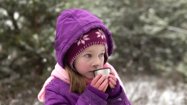 Egy téli ruhás kislány forró teát iszik egy utcai csészéből, a gőz megy. Közelkép.. — Stock videók