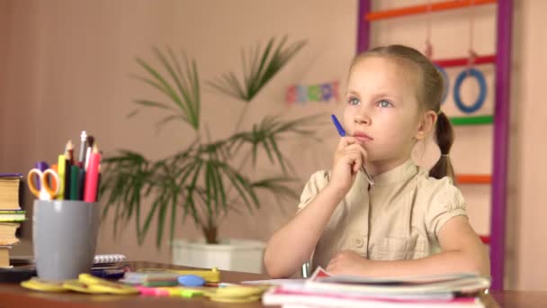 L'enfant d'âge préscolaire réfléchit en étant assis à la table. Elle fait ses devoirs. 4k — Video