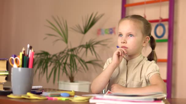 O pré-escolar está a pensar enquanto está sentado à mesa. Ela faz o trabalho de casa.4k — Vídeo de Stock