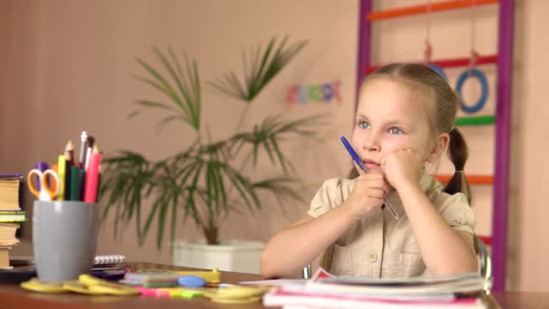 El niño en edad preescolar está pensando mientras está sentado en la mesa. Ella hace su tarea.. — Vídeos de Stock