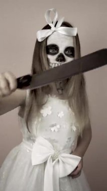 Yüzü boyalı küçük bir kız elinde satırı tutuyor. Korkuyor ve bıçak sallıyor..