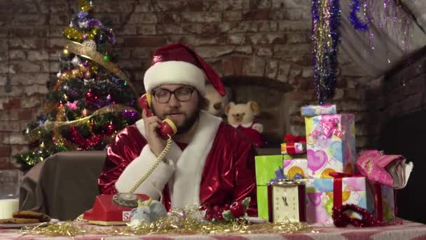 Père Noël drôle parle sur le vieux téléphone rouge tout en étant assis sur le canapé. Il répond à l'appel. — Video