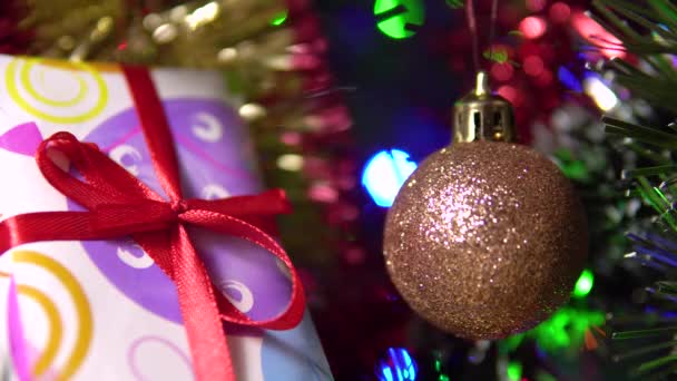 Una mano di bambini prende un piccolo regalo incartato con un nastro rosso da sotto l'albero di Natale.4k — Video Stock