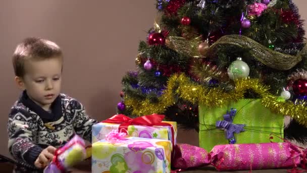 Маленький хлопчик кладе подарунки в ящики під Різдвяну ялинку. Різдвяні прикраси. Нові роки відпустки — стокове відео