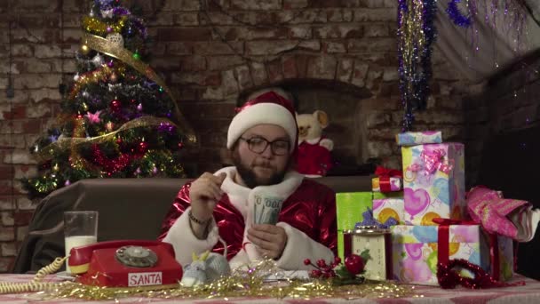 Grappige Kerstman zit op de bank telt een bundel van honderd dollar biljetten. — Stockvideo