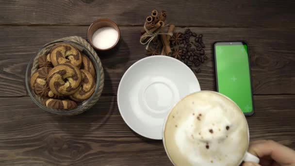 Una mano femminile preme sullo schermo verde dello smartphone sdraiato sul tavolo con una tazza di caffè. — Video Stock