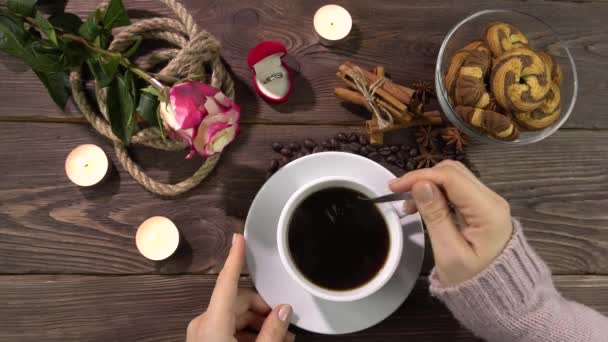 Frau rührt heißen Kaffee mit einem Löffel.Tisch mit Kerzen, Rose und Goldring in einer Geschenkbox .4k — Stockvideo