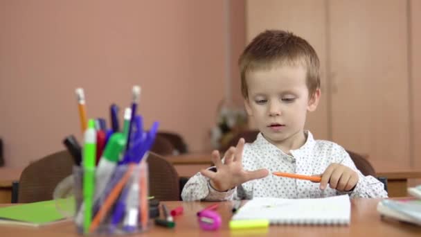 Seorang anak laki-laki tampan duduk di meja dan menghitung jari-jarinya di hand.Preschool pendidikan. — Stok Video
