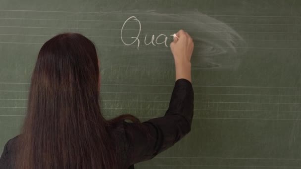The young teacher writes quarantine on the blackboard, turns and puts on a medical mask. — Stock Video