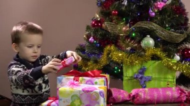 Küçük bir çocuk Noel ağacının altındaki kutulara hediyeler koyar. Noel süslemeleri. Yeni yıl tatili