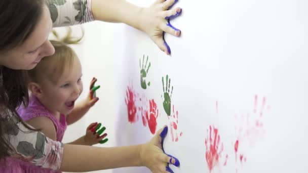 Mamá y su hija hacen huellas de manos usando pinturas en papel blanco.. — Vídeos de Stock