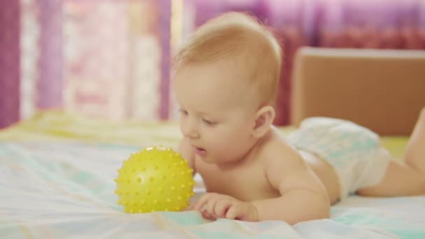 Um lindo bebé mente. Ele segura a bola na mão e brinca com ela.. — Vídeo de Stock
