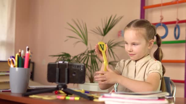 Una niña preescolar muestra signos con letras, mira en un teléfono inteligente, responde a una pregunta. — Vídeos de Stock