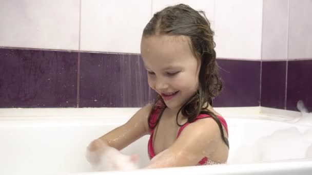 Una niña se lava la espuma en la ducha. Ella está sentada en un baño de burbujas. — Vídeos de Stock