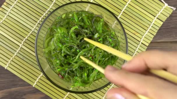 Chuka seaweed is raised with chopsticks by a womans hand.Chuka seaweed in a glass bowl stands. — Stock Video