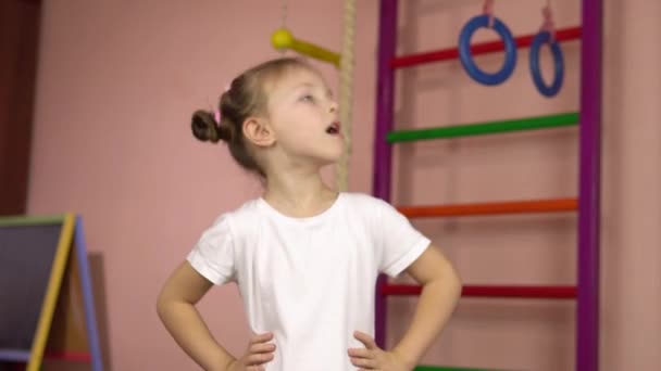 Pequena menina bonita em uma camiseta branca realiza a rotação da cabeça exercício físico.Esportes em casa. — Vídeo de Stock