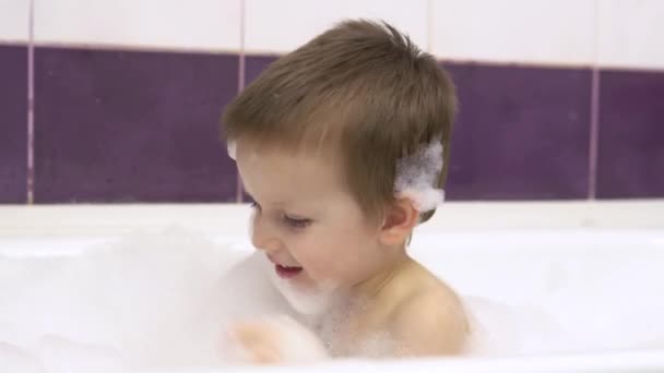 A kis jóképű fiú fürdik a kádban, sok habbal. Közelkép. Játékokkal játszik.4k — Stock videók