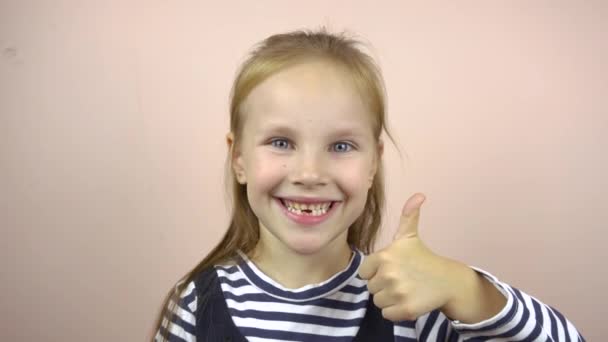 A beautiful girl of five to six years old shows a thumbs up gesture, smiles and grimaces. — Stock Video