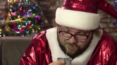 Noel Baba gibi giyinmiş genç bir adam elinde küçük bir marihuana filizi tutuyor.