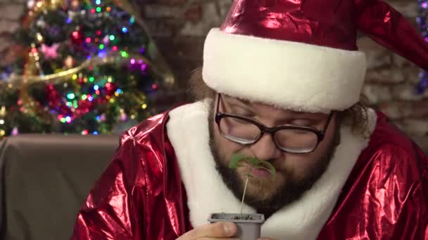 Молодой человек, одетый как Санта-Клаус держит в руках маленький росток марихуаны и гримаса.4k — стоковое видео