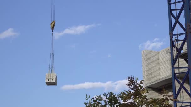 建設クレーンは、建設現場に負荷を輸送します。未完成の白いレンガ造りの建物. — ストック動画