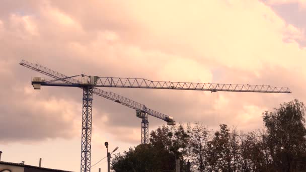 Rotace stavebního jeřábu na pozadí západu slunce s mraky. Dva jeřáby. — Stock video