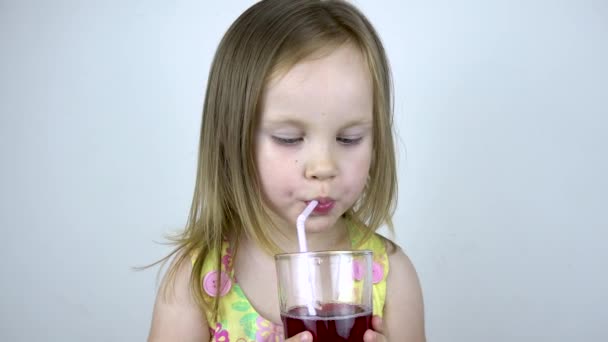 Tříletá holčička pije džus ze skleněného kelímku se slámou. Na bílém pozadí — Stock video