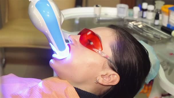Mujer joven recibiendo blanqueamiento UV en la oficina de dentistas por una máquina ultravioleta. — Vídeo de stock