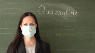 Tıp maskeli genç bir öğretmen okul yönetim kurulunda yazılı karantinayla duruyor ve kameraya bakıyor..