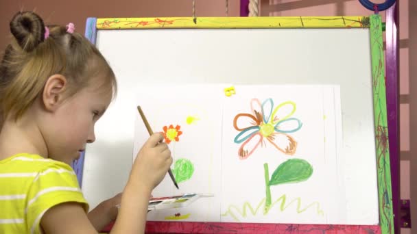 Kleines Mädchen von fünf Jahren zeichnet eine Blume in Aquarellen auf einer Staffelei. Kindergarten, Malstunde. — Stockvideo